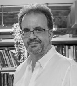 Here is a black and white photograph of a BGA webinar speaker smiling, wearing glasses and a white shirt with an unbuttoned collar.