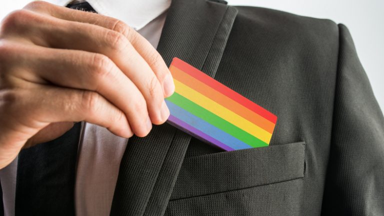 Close up of a business professional putting pride colours, LGBT+ card into the chest pocket of a smart black blazer.