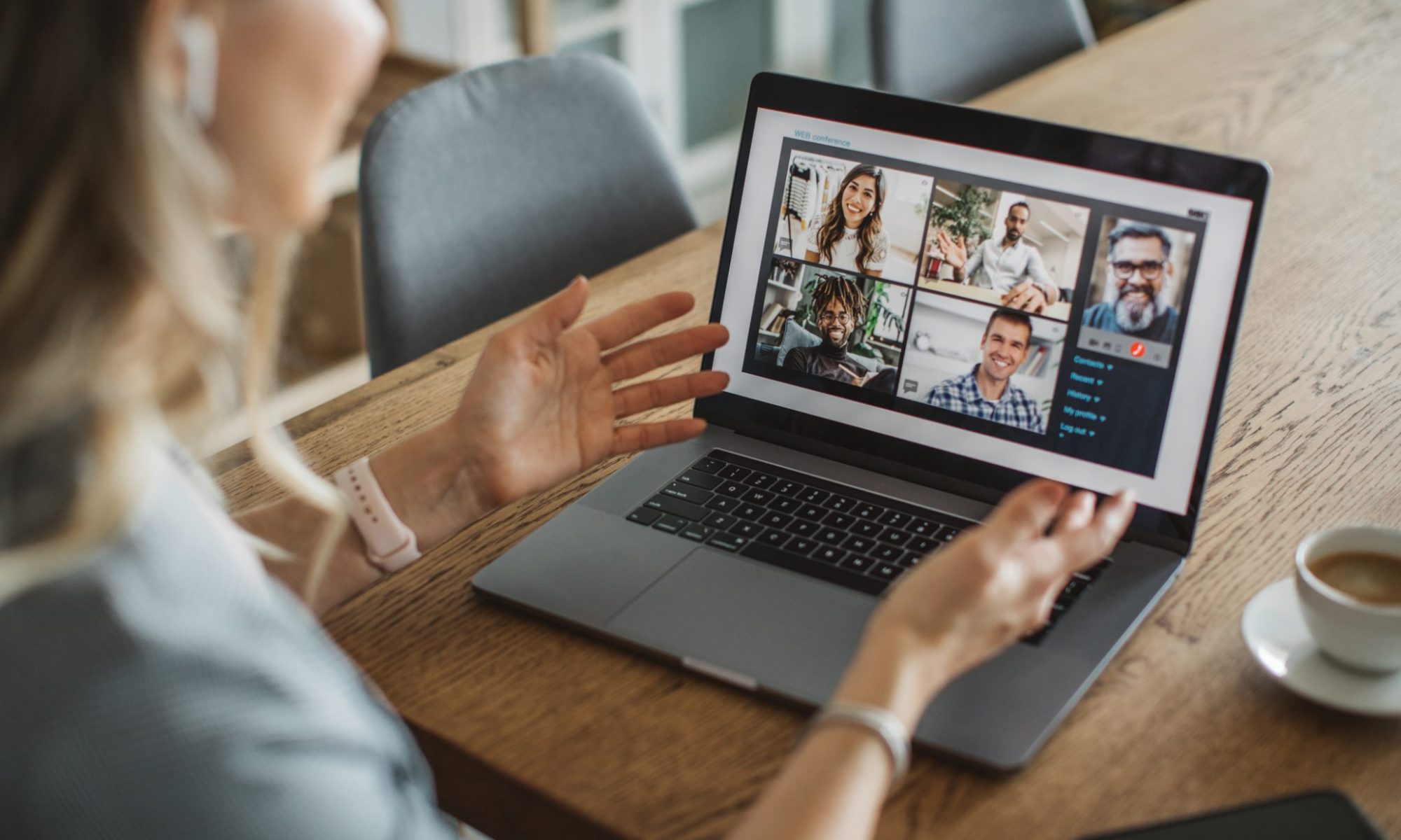 A person is having a remote team meeting on the laptop. The individual is working from home engaging with peers. Next to her laptop sits a small shot of espresso.