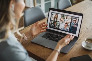 A person is having a remote team meeting on the laptop. The individual is working from home engaging with peers. Next to her laptop sits a small shot of espresso.