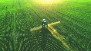 A tractor watering crops with a sprinkler system on a sunny day.