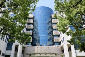 The Glorious Sun School of Business and Management at Donghua University is a cylinder glassed building framed around green trees.