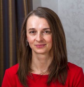 The Executive Director, Faculty of Business Administration, Prague University of Economics and Business and speaker from the AMBA & BGA Accreditation Forum smiling. The Executive Director has medium length brown hair with brown eyes, wearing a bright red outfit with dangling oval-shaped earrings.