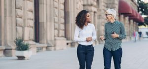 Here are two female business professionals engaged in a conversation and walking outside down a path.