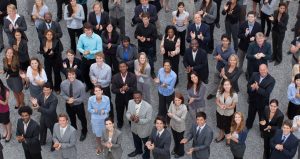 Here is a large, diverse crowd of business working professionals socially distancing standing outside dressed in smart attire.